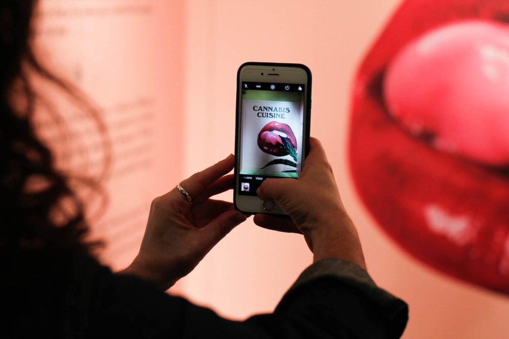 Une femme prenant une photo de l'affiche de la "cuisine de cannabis" avec son téléphone portable à l'exposition