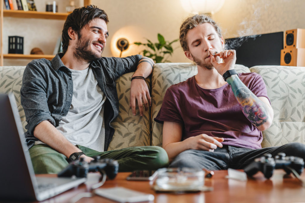 Dos jóvenes sentados en un sofá fumando un porro