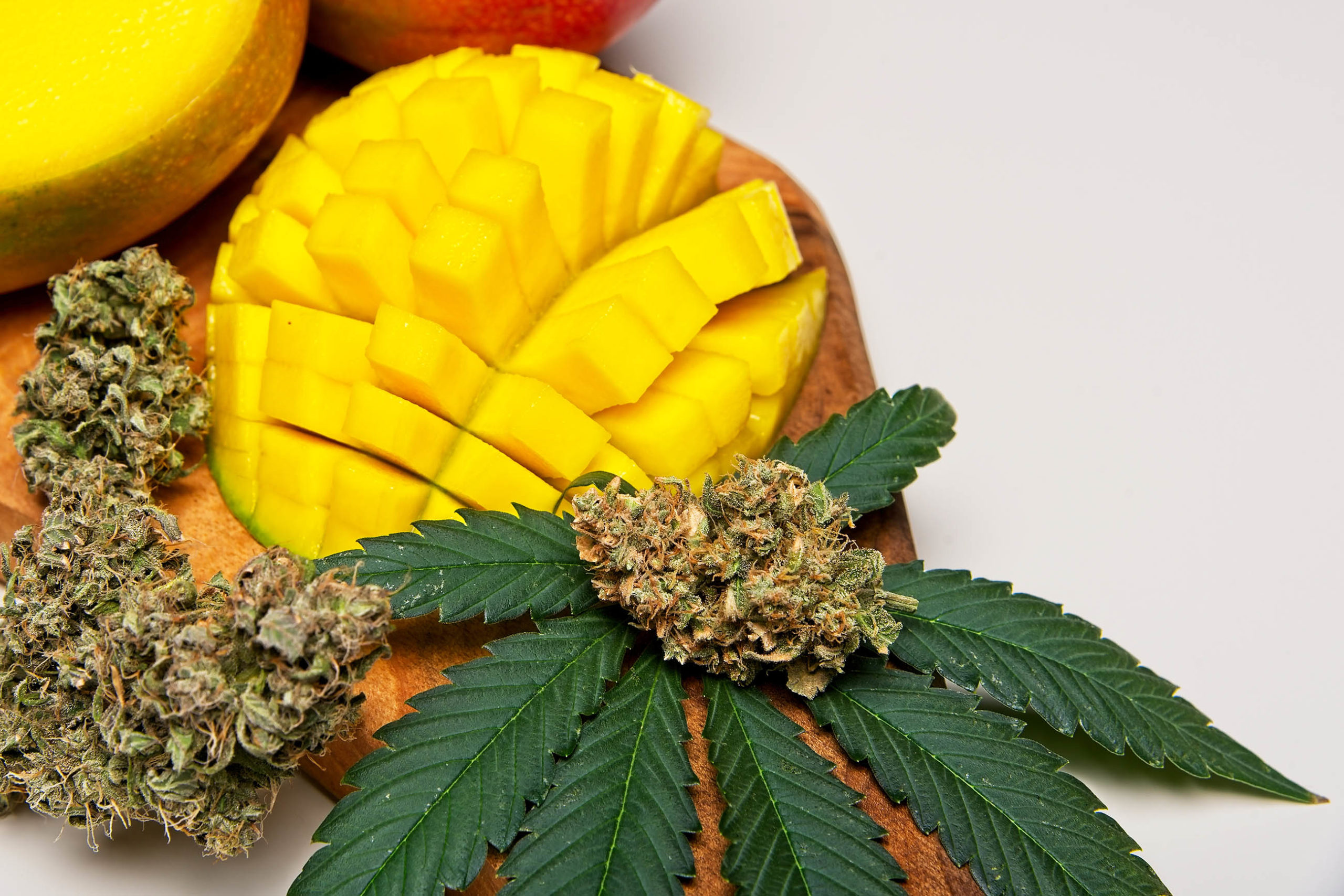 Mango in tweeën gesneden met cannabisbladeren en gedroogde cannabisbloemen op een snijplank