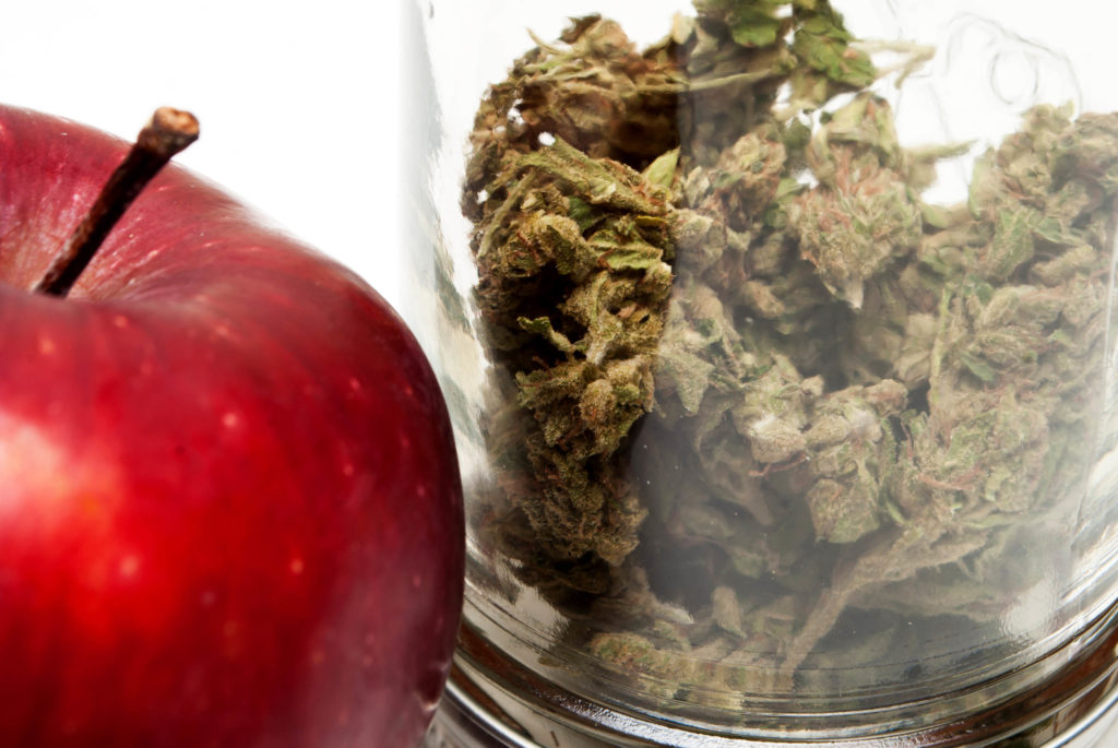 Manzana roja y un frasco con flores de cannabis secas contra el fondo blanco