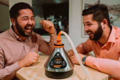 Two men sitting on at the table laughing and a vaporizer on the table