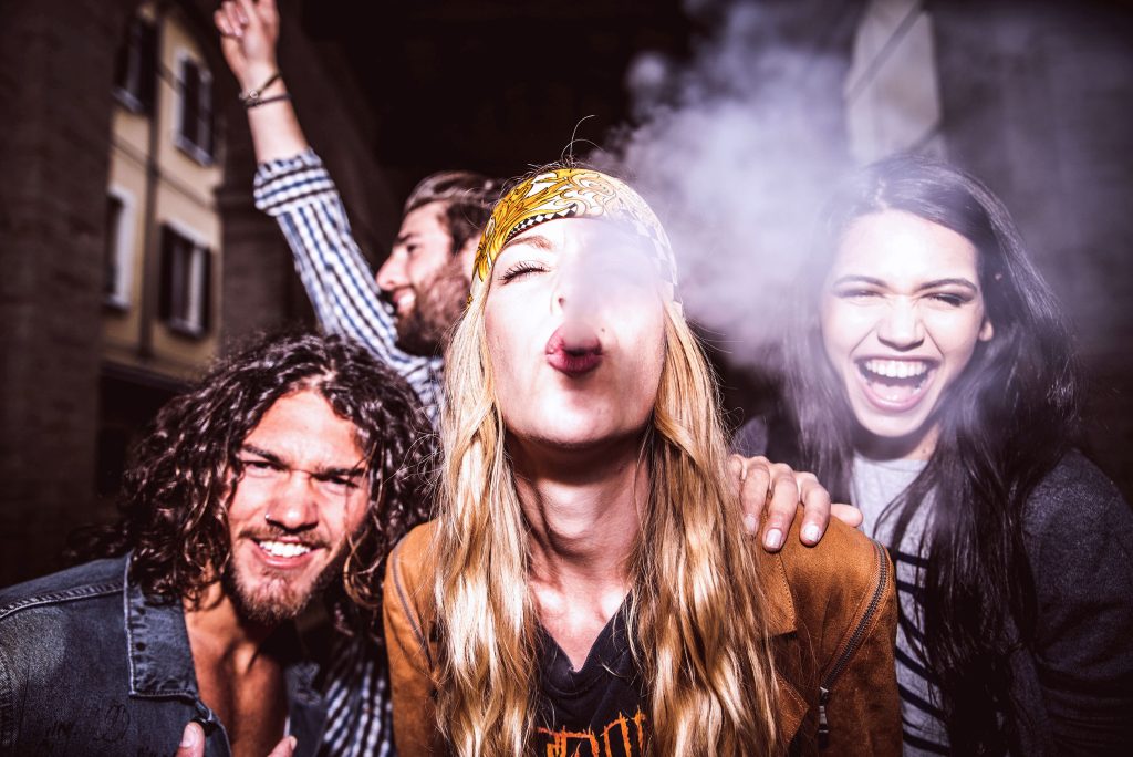 A group of young people having fun and a blonde girl blowing a smoke