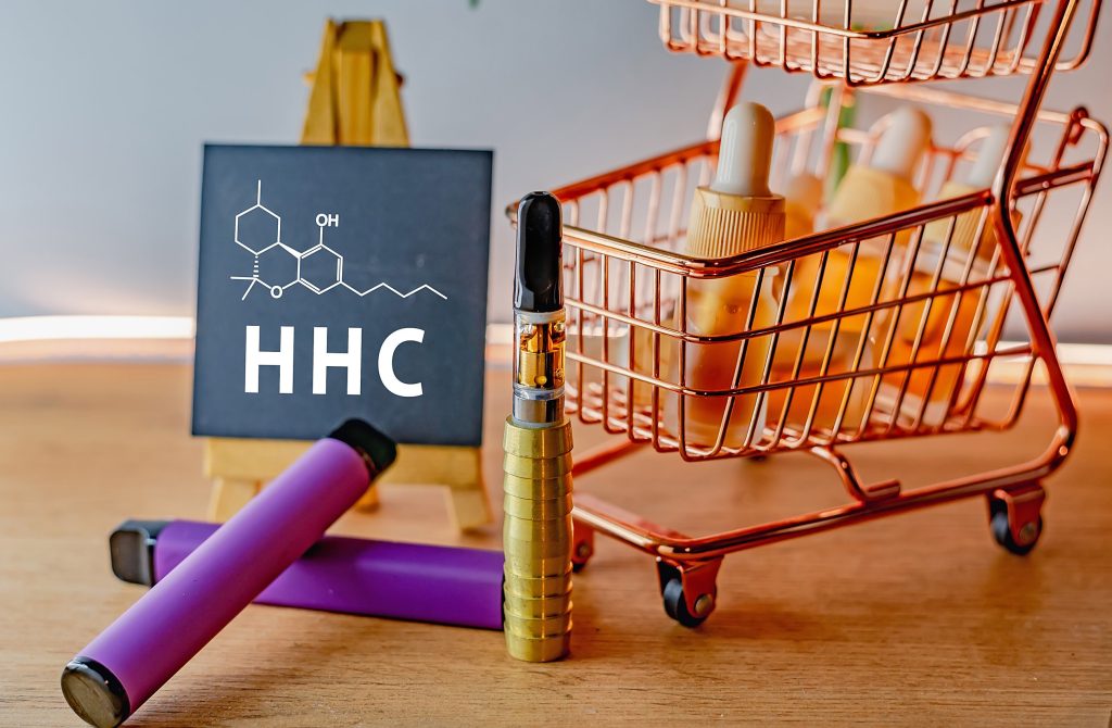 Miniature shopping charts with cannabis extracts, vape pens and a blackboard with HHC chemical formula beside