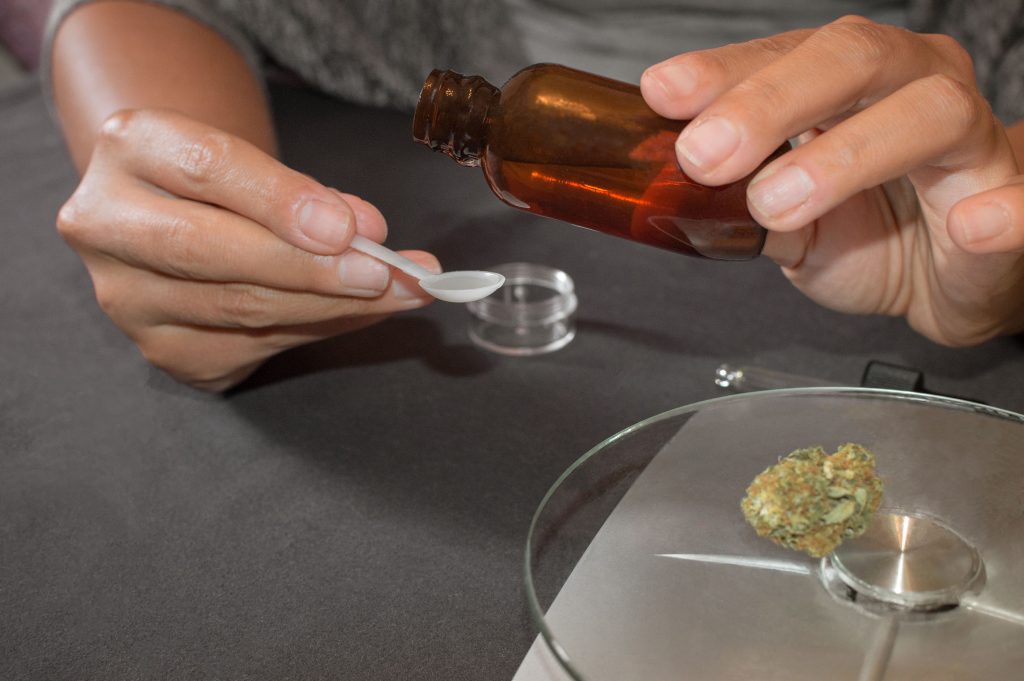 A person dosing a cannabis tincture from a glass bottle and dried cannabis on a scale