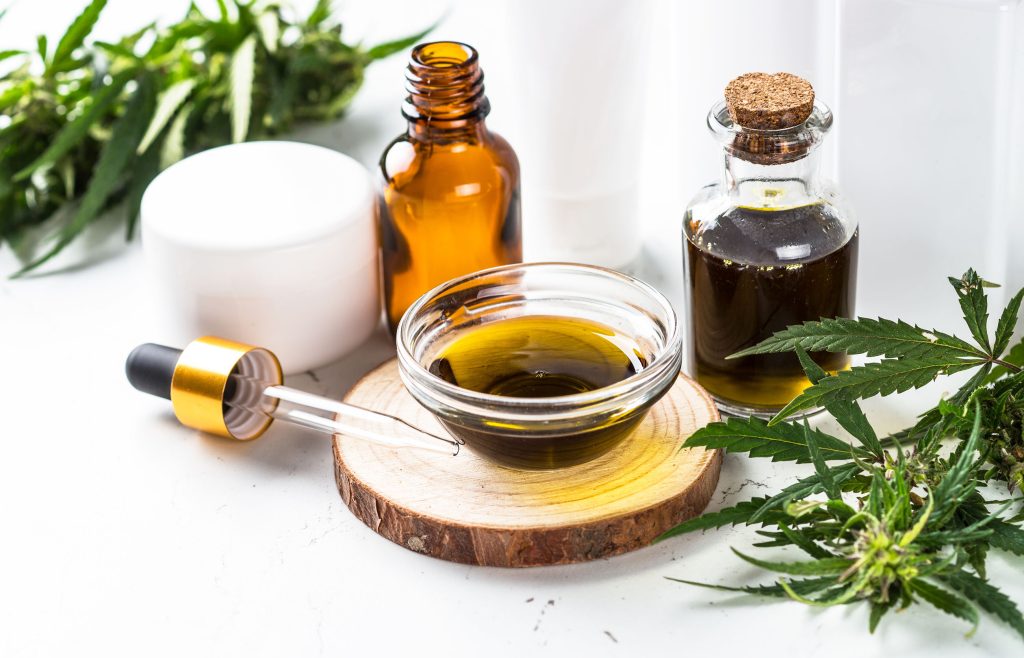 Cannabis tincture in a glass cup, with a pipette, glass bottles and cannabis leaves beside