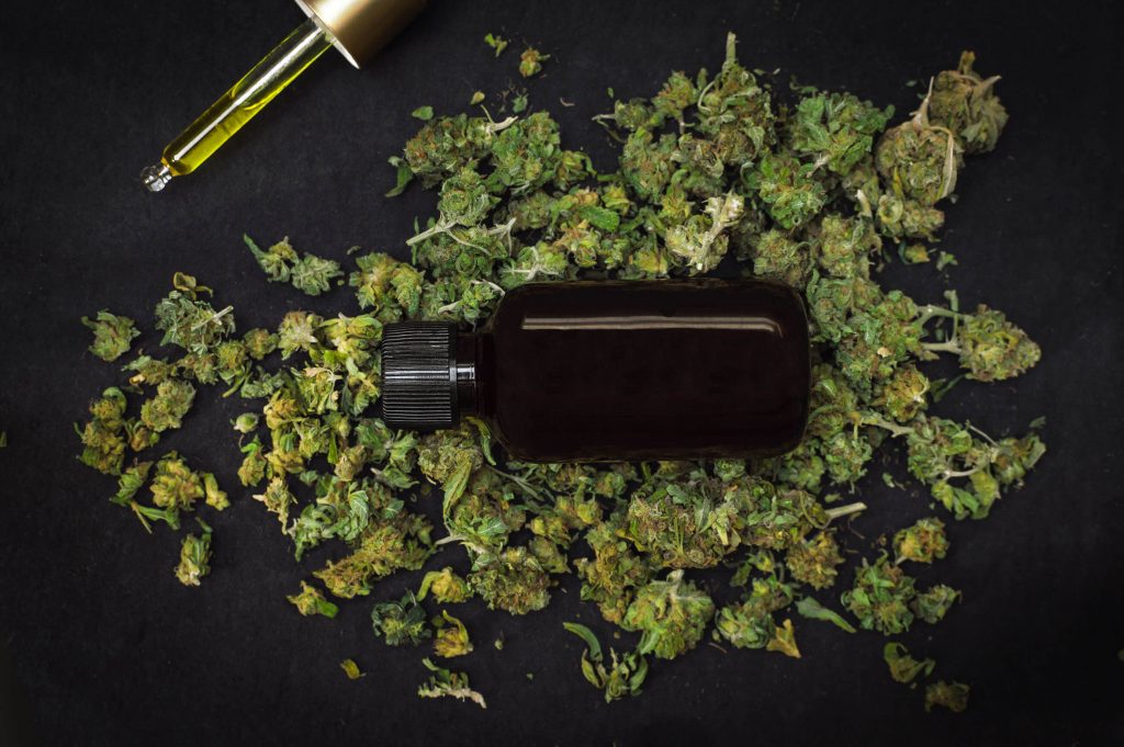 A dark glass bottle and a pipette with cannabis tinctures and dried cannabis flowers around