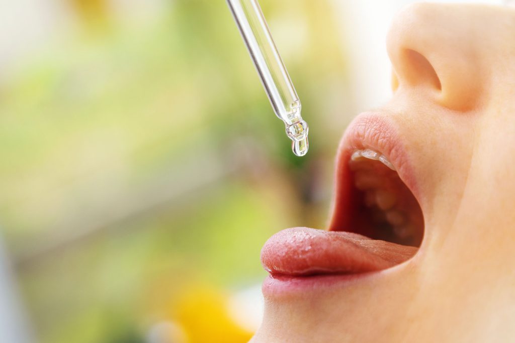 A person with opened mouth ready to take cannabis tincture via pipette