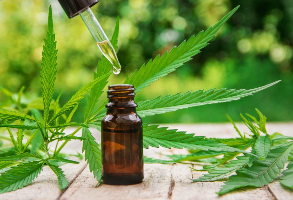 Pipette with cannabis tincture and a dark glass bottle with cannabis leaves in the background