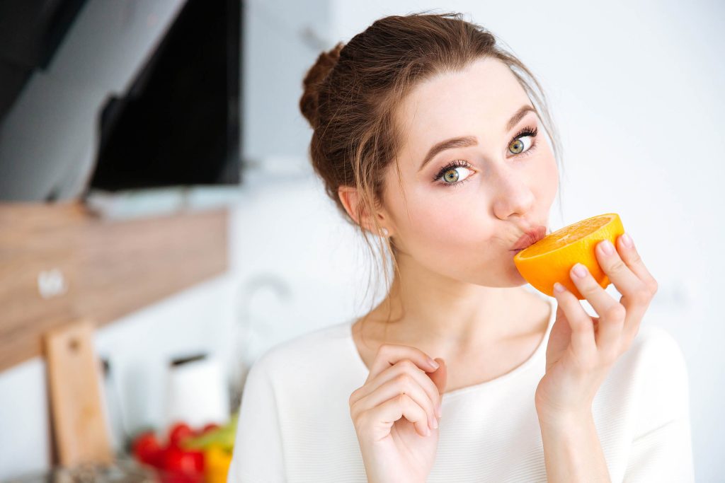 Una mujer que come una naranja que está cortada por la mitad