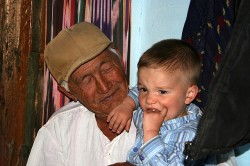 An elderly man wearing a beige cap holding a young child