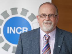 Professor Wayne Hall standing in front of the International Narcotics Control Board logo